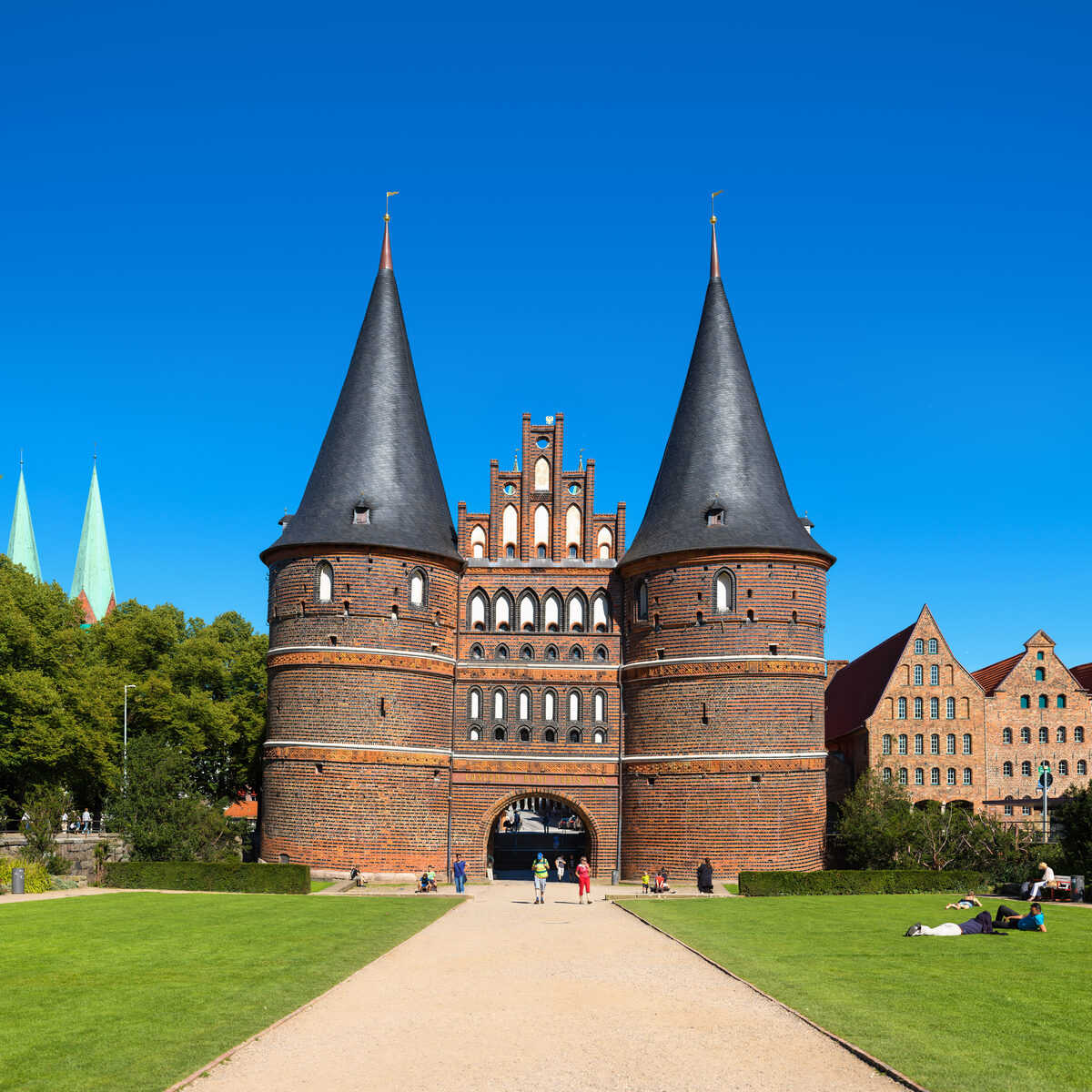 Das Holstentor in Lübeck mit Grünflächen, Weg und historischen Salzspeichern